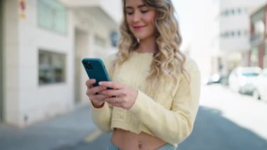 Sokakta akıllı telefon kullanan, kendine güvenen genç sarışın kadın.