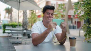 Young hispanic man smiling confident looking video on smartphone at coffee shop terrace