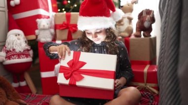 Sevimli İspanyol kız hediyesini açıyor. Evdeki Noel ağacının yanında oturuyor.