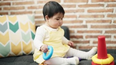 Adorable hispanic baby playing with hoops sitting on sofa at home