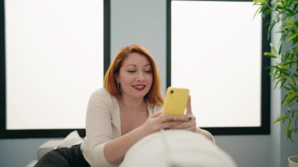 Νεαρή Κοκκινομάλλα Γυναίκα Που Χρησιμοποιεί Smartphone Κάθεται Στον Καναπέ Στο — Αρχείο Βίντεο