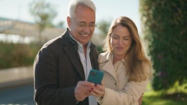 Orta yaşlı çift parkta akıllı telefon kullanarak gülümsüyor.
