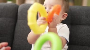 Adorable toddler playing with hoops sitting on sofa bitting hoop at home