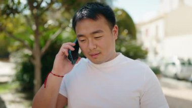 Akıllı telefondan konuşan genç Çinli bir adam parkı gözetliyor.