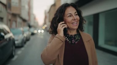 Orta yaşlı İspanyol kadın gülümsüyor. Akıllı telefondan konuşuyor.