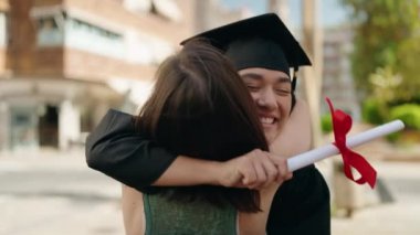 Two women mother and graduated daughter holding diploma kissing at street