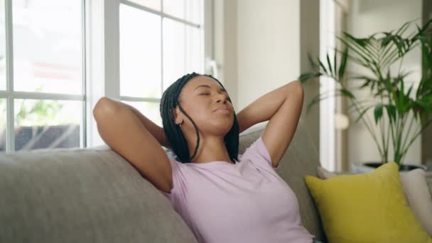 非洲裔美国妇女放松了 双手放在头上 坐在家里的沙发上 — 图库视频影像