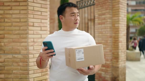 若い中国人男性宅配便使用スマートフォン保持パッケージでストリート — ストック動画