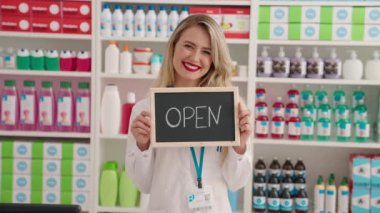 Young beautiful hispanic woman pharmacist smiling confident holding open blackboard at pharmacy