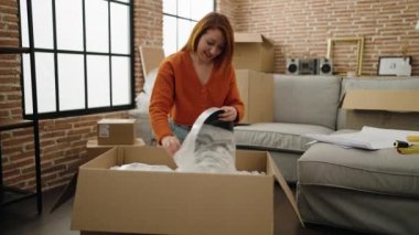 Young redhead woman smiling confident unboxing watch at new home