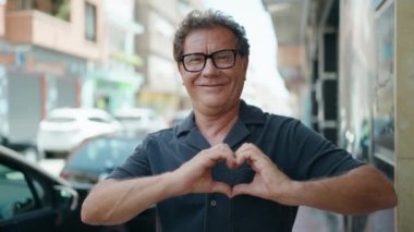Middle age man smiling confident doing heart gesture with hands at street