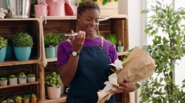 Afrikalı Amerikalı kadın çiçekçi çiçekçiye elinde çiçeklerle akıllı telefondan konuşuyor.