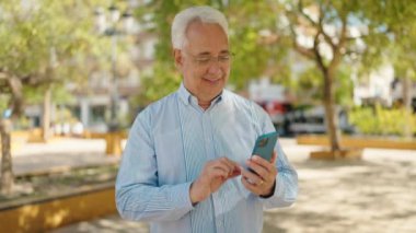 Son sınıf öğrencisi kendinden emin gülümsüyor. Parktaki akıllı telefonun yanında özçekim yapıyor.