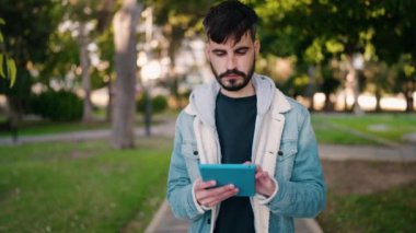 Young hispanic man smiling confident using touchpad at park