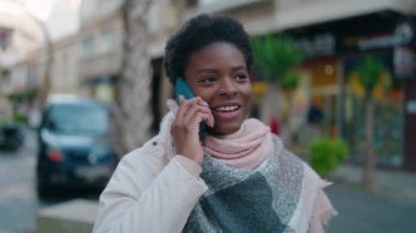 Genç Afrikalı Amerikalı kadın gülümsüyor. Kendine güveni tam. Sokakta akıllı telefondan konuşuyor.