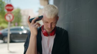 Young caucasian man listening audio message wearing headphones at street