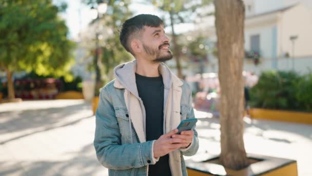 Молодий Іспаномовний Чоловік Посміхається Впевнено Роблячи Фотографії Смартфона Парку — стокове відео