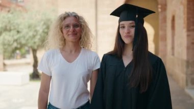 Two women mother and graduated daughter standing with arms crossed gesture at campus university