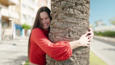 Young woman smiling confident hugging tree at park