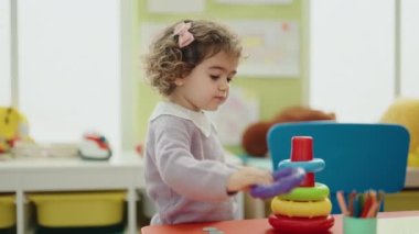 Adorable hispanic girl playing with hoops toys standing at kindergarten
