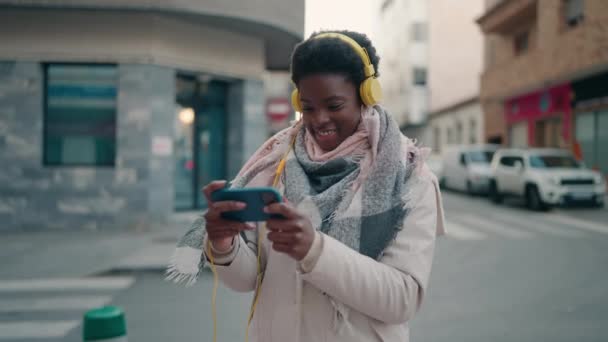 Young African American Woman Playing Video Game Using Smartphone Headphones — Stock video