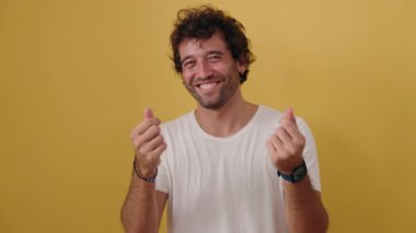 Young hispanic man smiling confident doing spend money gesture over isolated yellow background