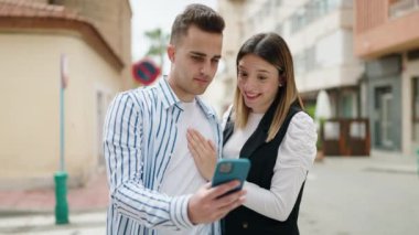 Man and woman couple hugging each other using smartphone at street