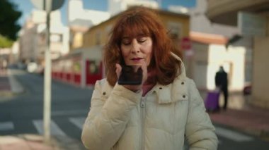 Middle age redhead woman smiling confident sending audio message at street