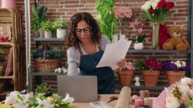 Middle age woman florist using laptop reading document at flower shop