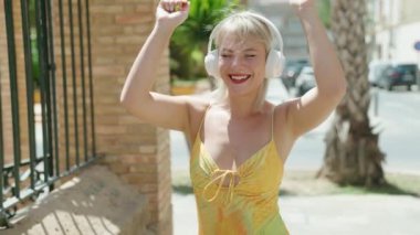Young blonde woman listening to music and dancing at street