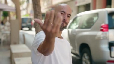 Young bald man smiling confident doing coming gesture with hand at street