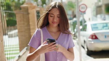 Genç, güzel, İspanyol bir kadın gülümsüyor ve caddede akıllı telefondan konuşuyor.