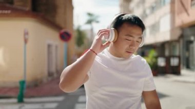 Young chinese man smiling confident listening to music at street