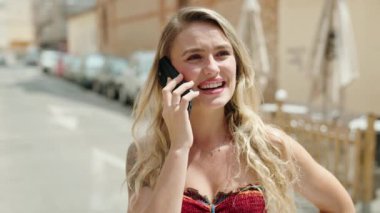 Genç sarışın kadın gülümsüyor. Kendine güveni tam. Akıllı telefondan konuşuyor.