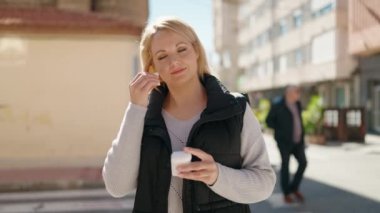 Genç sarışın kadın sokakta kablosuz kulaklık kullanarak müzik dinliyor.