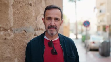 Orta yaşlı bir adam sokakta kendine güvenerek gülümsüyor.