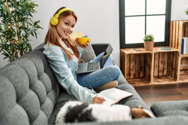 Kanepede oturan beyaz bir kadın ve evde ders çalışan bir köpek.