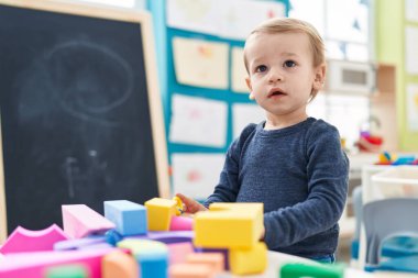 Anaokulundaki masada oturan sevimli sarışın çocuk geometri bloklarıyla oynuyor.