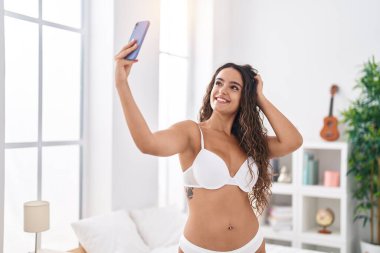 Genç ve güzel İspanyol kadın yatak odasında akıllı telefonuyla selfie çekiyor.