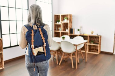 Orta yaşlı, kır saçlı, turist bir kadın sırt çantasıyla evde bekliyor.