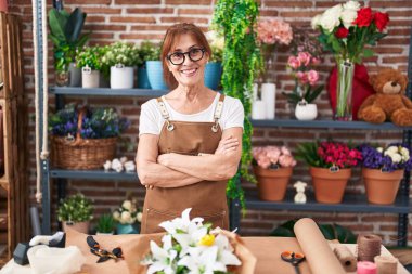 Middle age woman florist smiling confident standing with arms crossed gesture at flower shop