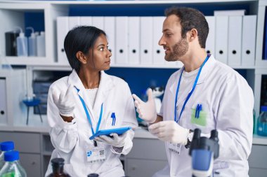 Man and woman scientists using touchpad holding sample at laboratory