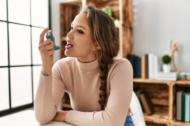 Evdeki masada oturan, astım spreyi kullanan genç, güzel İspanyol kadın.