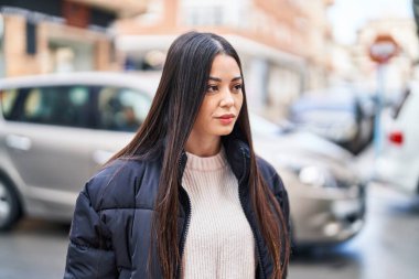 Young beautiful hispanic woman looking to the side with relaxed expression at street