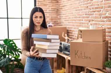 Young woman holding books at home skeptic and nervous, frowning upset because of problem. negative person. 
