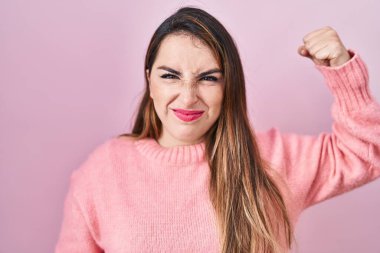 Young hispanic woman standing over pink background strong person showing arm muscle, confident and proud of power 