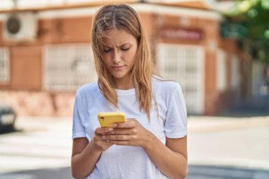 Young blonde girl using smartphone at street