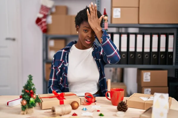 stock image African american woman working at small business doing christmas decoration surprised with hand on head for mistake, remember error. forgot, bad memory concept. 