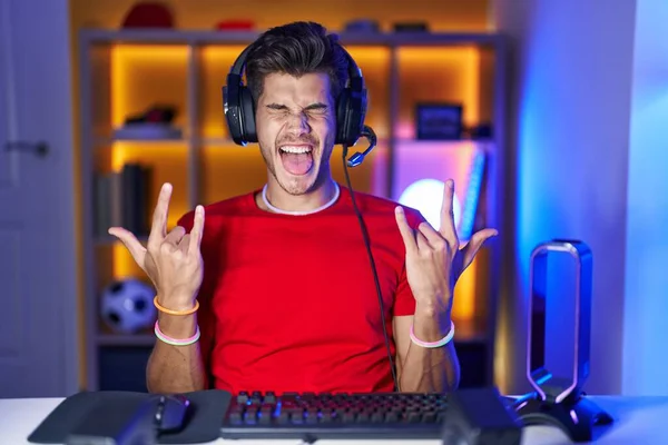 若いヒスパニック系の男が手を上げて岩のシンボルをやって狂気の表現で叫んでビデオゲームをプレイ 音楽スター 重い概念は — ストック写真