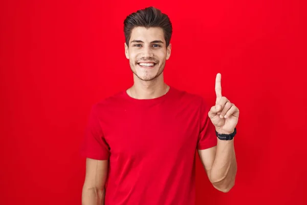自信と幸せ笑みを浮かべている間に赤い背景が表示され 指の第一位を指して立って若いヒスパニック系の男 — ストック写真